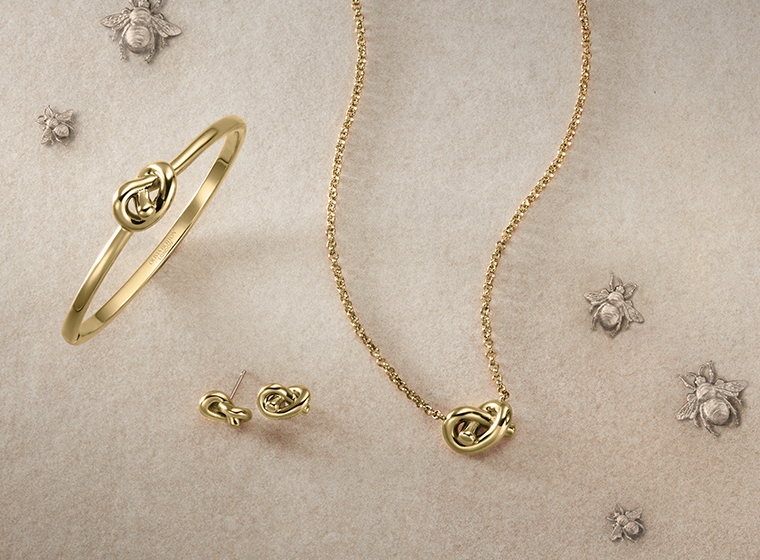 a gold necklace, bangle and matching earrings set displayed on a cream background  