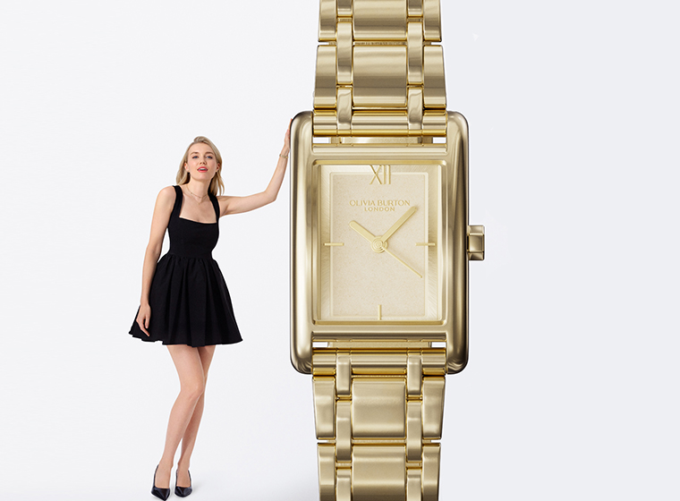 A women with blonde hair in a black dress stood next to a gold rectangle watch