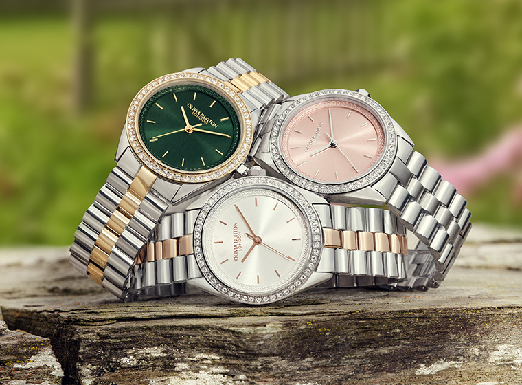 3 watches sat on a block of wood on a garden background 