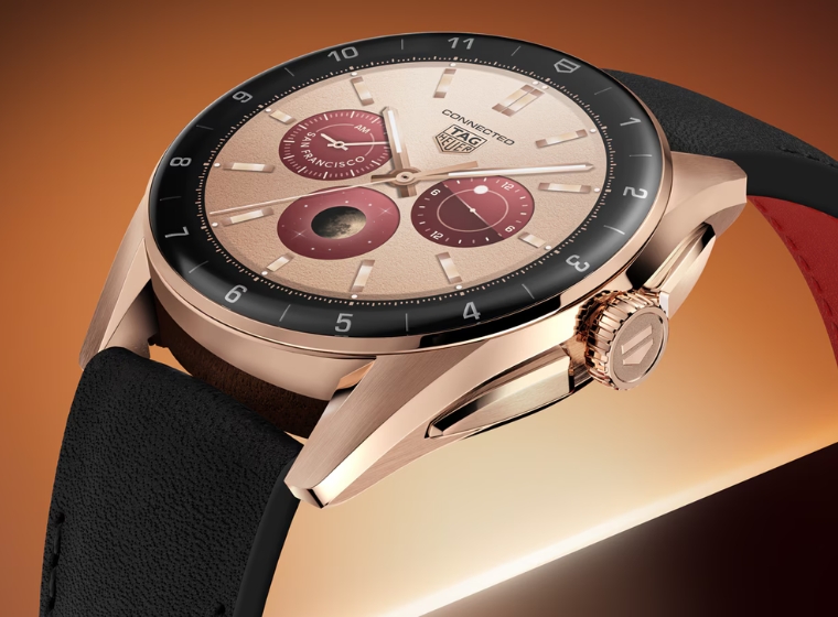 Rose gold coloured TAG smartwatch with a black and red strap on a golden background
