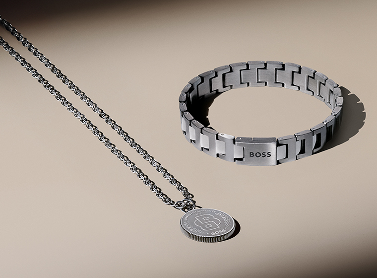 BOSS grey tone curb necklace and bracelet set on a bronze background 