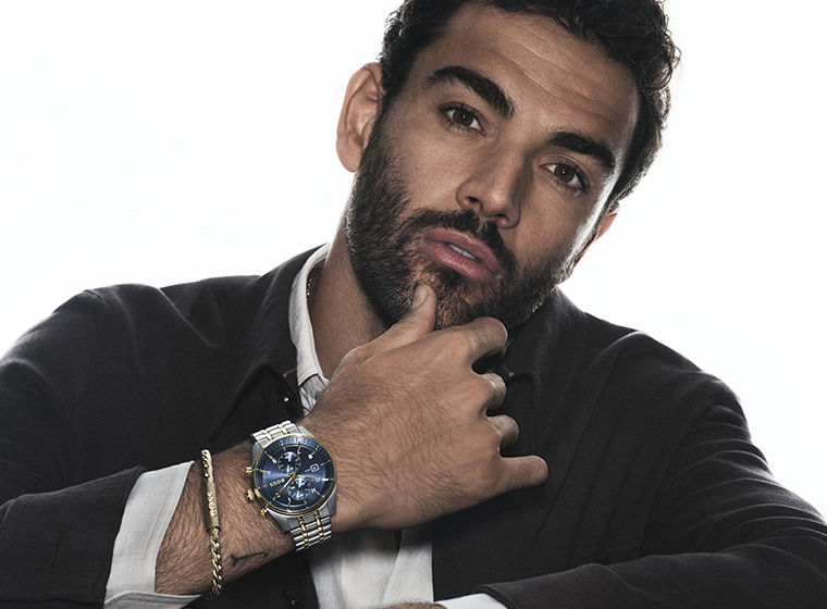 Man in a black jumper with dark hair and beard wearing a silver watch with a blue dial watch and steel bracelets  