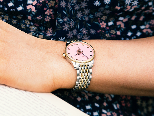 A close up of a pink dial watch on a womens arm, whilst reading a book