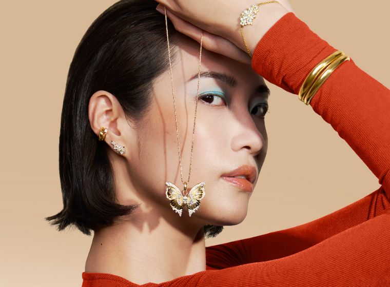 Model wearing a red top holding a gold butterfly necklace near her face