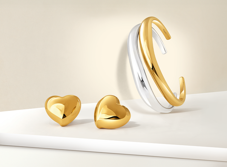 Gold heart earrings displayed near a sliver and gold bangle 